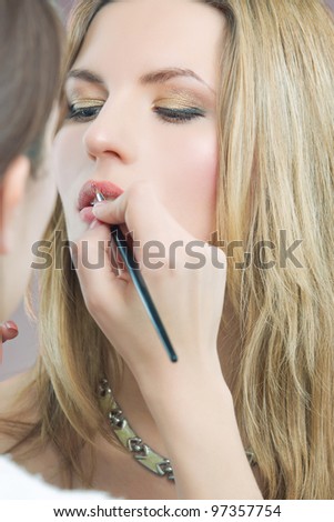 makeup artist doing makeup with a brush to young blonde woman