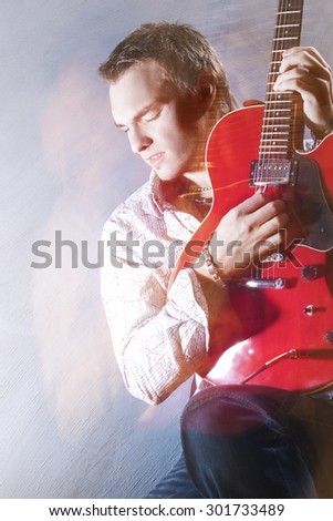 Music Concepts. Portrait of Young Male Guitar Player Performing with Guitar against Gray. Mixed Light Used. Vertical Image Composition