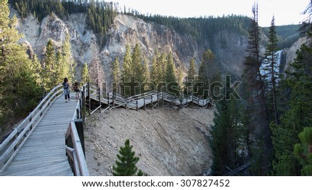 A mother and daugher walk hand in hand down a wooden boardwalk in the canyon to view the lower Yellowstone  Falls, at Yellowstone National Park.