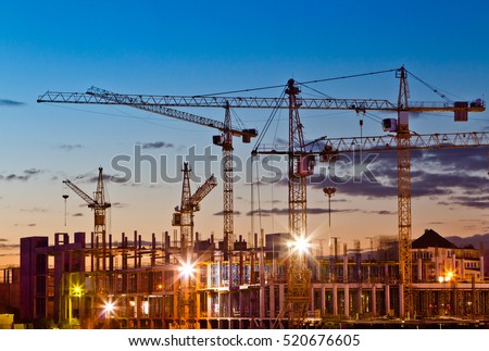 Silhouettes of tower cranes against the evening sky. House under construction. Industrial skyline
