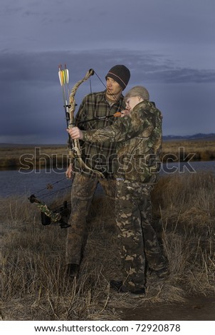 A young boy learns bow hunting from his father.