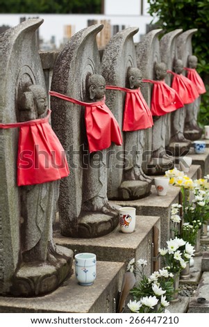 Stone statues at an asian cemetery with a red material wrapped around and flowers at the base of the stone