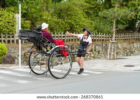 June 2012 - Arashiyama, Japan: An asian man pulling a Pulled rickshaw with two people seating and moving away from the camera