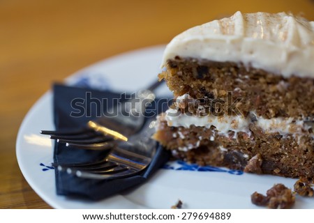 A close-up of a carrot cake on a white plate with a blue logo and two forks on the side