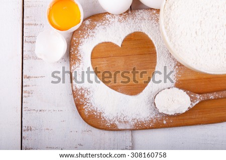 Heart of flour on wooden board on a kitchen table with a bowl of flour and eggs. Cooking