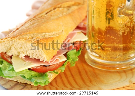 baguette sandwich closeup made of lettuce, tomatoes, ham, and cheese whit a glass of beer
