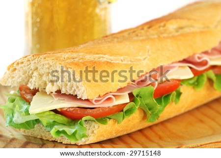 baguette sandwich with lettuce, tomatoes, ham, and cheese with a glass of beer in the background
