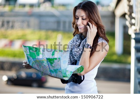 young woman tourist holding paper map outdoors and talking by the phone