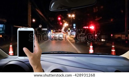 Man using cell phone while driving, blur image of police checkpoint at dark night as background.