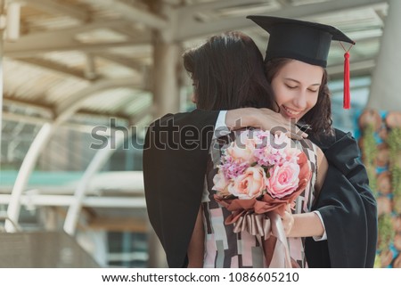 Mother congratulations, hug, give flower to daughter. Two girls hug and congratulations each other at the university. They are graduates and hold diploma certificate. They are happy and in good mood.