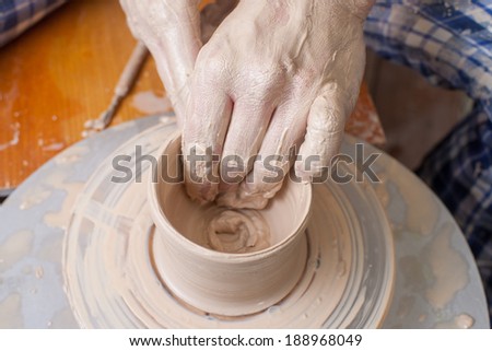 Hands of a potter, creating an earthen jar on the circle from white clay