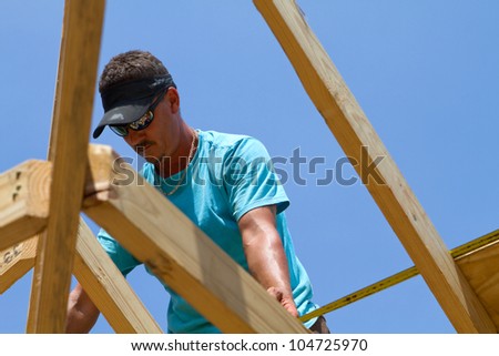 Carpenter uses a tape measure to calculate the length of the next sheathing board to cut for the roof.