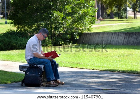 Mature college student studies a book while sitting on a bench at a state university campus.