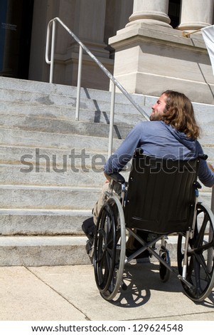 Disabled man in wheelchair looks for a ramp to gain access to a public building entrance.