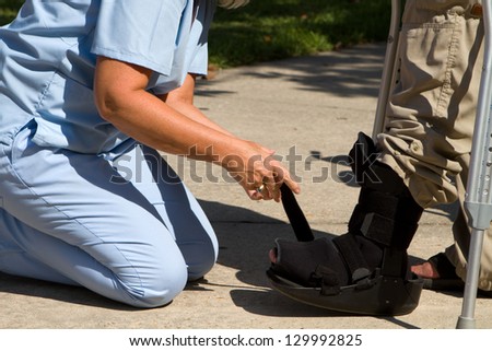 Female nurse adjusts strap on patient\'s ankle brace.