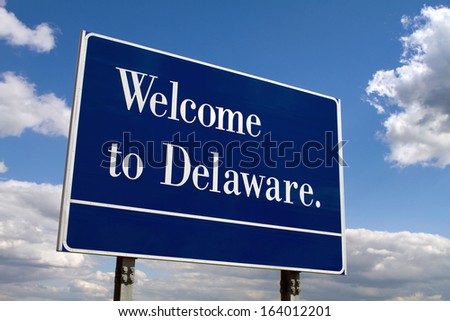 Welcome to Delaware sign on the state liNe against a cloudy blue sky.