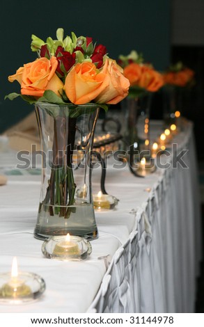 Bridesmaids bouquets sit in vases of water on the head table at a wedding reception.