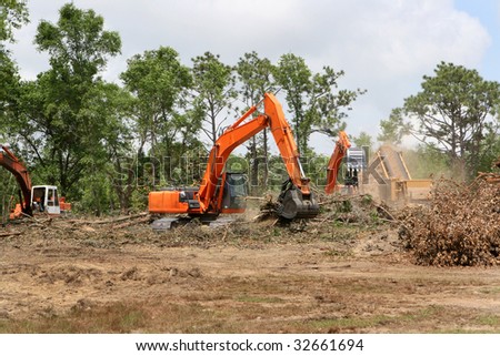 Backhoes operate clearing trees and brush from a construction site.