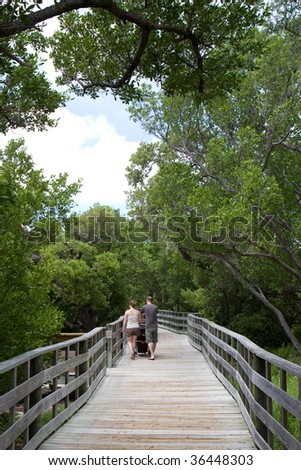 A young couple push a stroller along a raised wooden walkway in a preserve area of Anne\'s Beach in the Florida Keys.