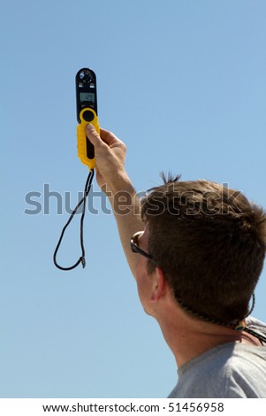 Man holds a handheld wind speed meter to check the velocity of the wind.