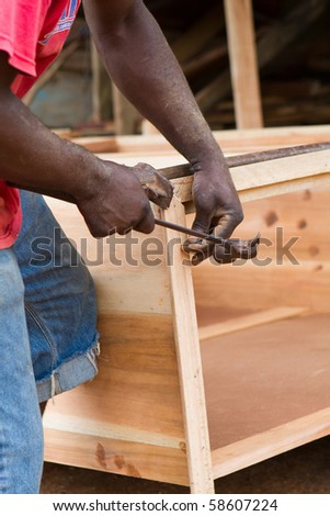 Black man uses hammer and nail to build a dresser chest out of cedar in Jamaica.