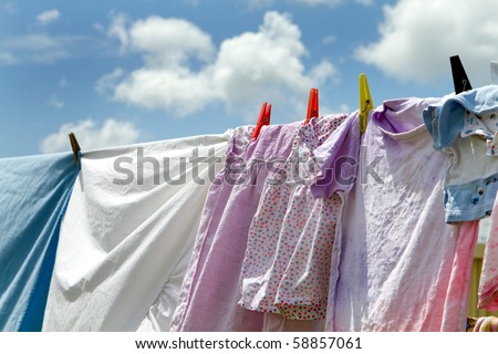 Children\'s clothes and bedsheets have been hung out to dry on a clothesline viewed against a blue sky with clouds.