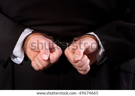 Close up of man wearing suit handcuffed behind his back.