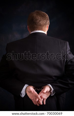 Businessman in suit is handcuffed behind his back.