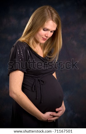Blonde expectant mother in the third trimester of pregnancy holds her abdomen and looks down contemplating her unborn child.