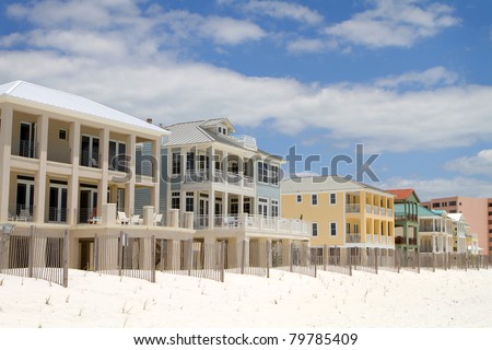 Expensive high end vacation beach homes and rentals built behind a small dune line and sand fences along the shoreline in Destin, Florida.