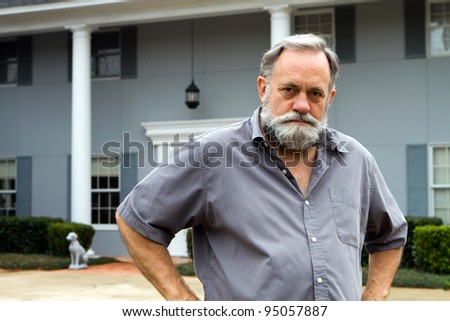 Unhappy homeowner poses in front of his two story columned southern home.