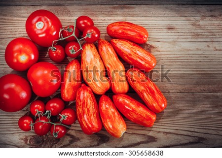 Different kinds of ripe tomatoes: speckled roman with yellow streaked, goose greek, cherry tomatoes on a green stem. Top view. On wooden background.