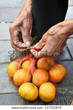 Old man's hands to tie a string bag of oranges for sale.
