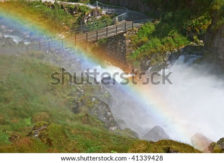 Rainbow over wet grass and stream of water.