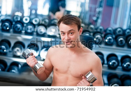 Muscular man lifting dumbbell in sport club