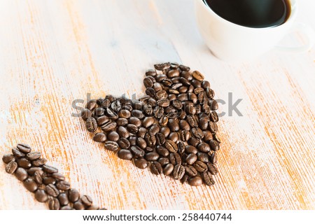 Heart shape made from coffee beans with a cup of coffee on a a wooden table desk spelling I love coffee