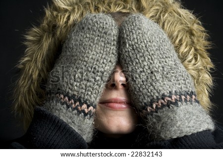 Happy young woman covering her eyes with gloved hands in winter