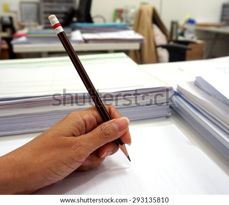 Women\'s hands grip a pencil writing on the white paper.