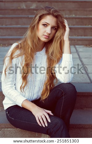 Young fashionable model with long blond hair sitting on the steps. Outdoor shot