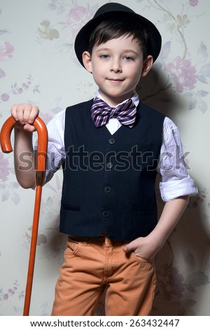 A young wizard with brown cane. A boy is wearing a light t-shirt with black waistcoat. The hat and striped bow tie complete his look.