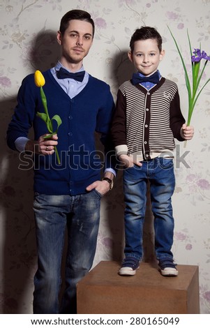 Two gentlemen: young father and his little cute son. man is holding yellow tulip. blue-eyed boy with purple flower. Studio shot
