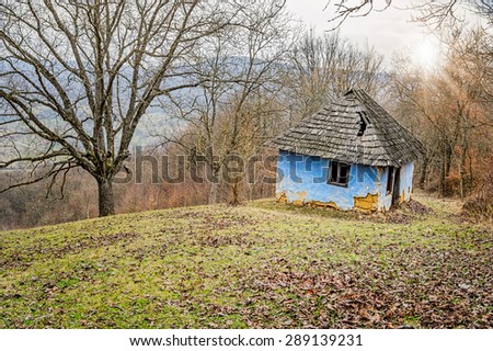 Ruined blue old house made of clay in the hills surrounded by trees and bathed in sunlight.