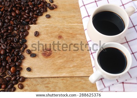 two white cups of black coffee placed on a napkin decorated with coffee beans on wooden background