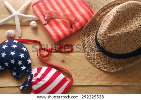bikini is striped american flag, brown hat and sunglasses put on red striped towel with shells and starfish are placed on a wooden background