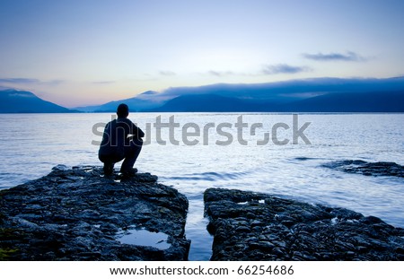 Man sitting on a small island watching the sunrise, slight cooling tone added.