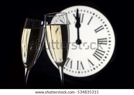 CELEBRATION OF THE NEW YEAR, glasses raising with champagne, background of the clock unfocussed