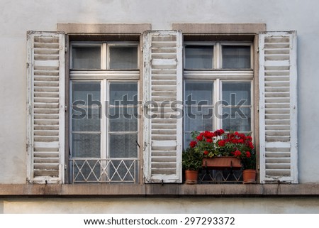 Old Windows with Shutters and Plants Two windows with opened shutters. Red geranium flowers in one of them.
