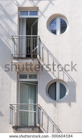 Modern Architecture and its Shadows\
Detail of a white building with two balconies and circle windows. Lines of the shadows on the wall. Reflection of the sky in the windows.