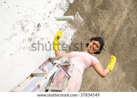 Strong and independent woman  standing on a ladder painting exterior wall