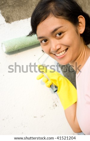 asian young woman happy with her painting job with roller and gloves